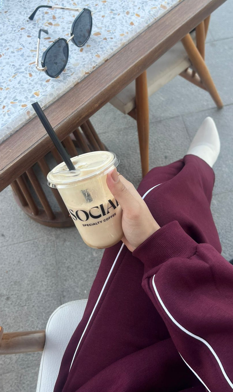 Person holding a cup with 'Society' branding outdoors, sitting at a table.